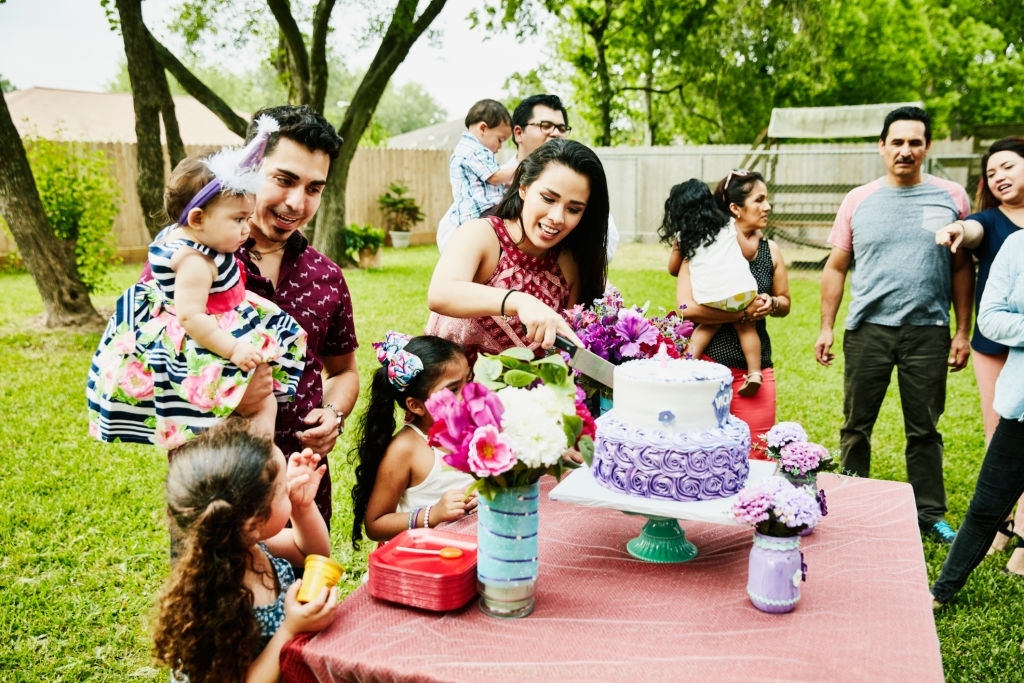 Couples gathered in a lawn with their kids to witness a lady cutting cake