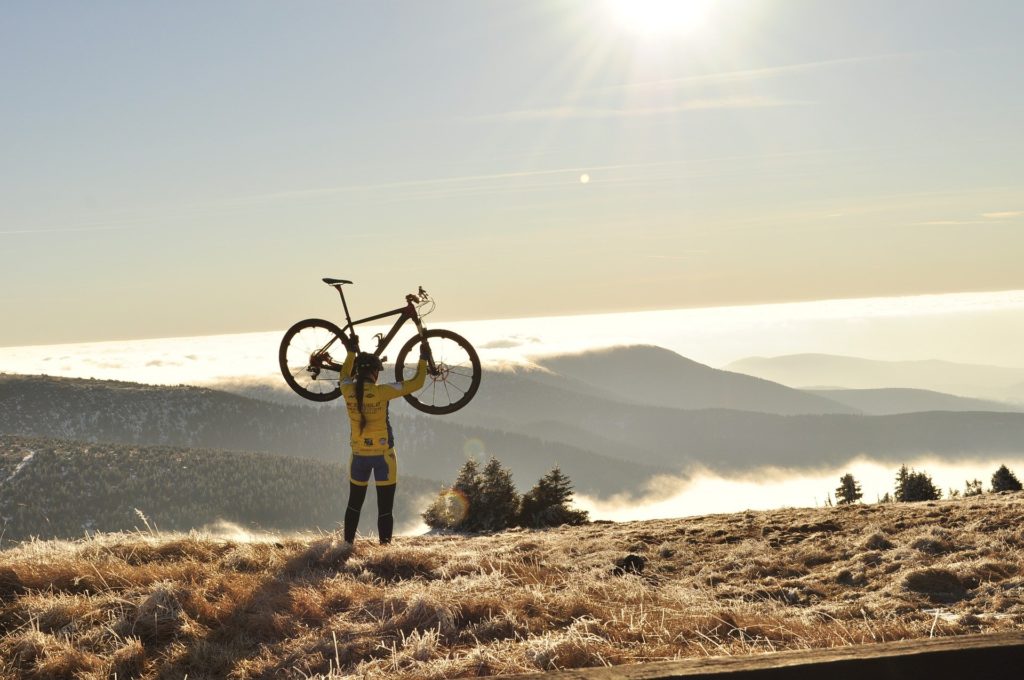 Woman lifting her cycle overhead on the top of a mountain 